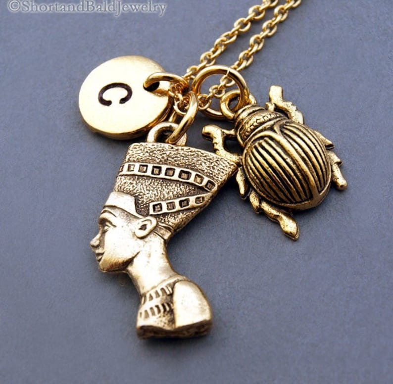 K&ouml;nnte beinhalten: Goldkette mit einem Anh&auml;nger einer &auml;gyptischen K&ouml;nigin, einem Skarab&auml;us-Anh&auml;nger und einem goldenen Initialanh&auml;nger mit dem Buchstaben C.