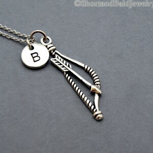 May include: Silver necklace with a bow and arrow charm and a letter B charm.