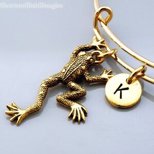 Könnte beinhalten: Goldarmband mit einem goldenen Frosch-Anhänger und einem goldenen Anhänger mit dem Buchstaben K.