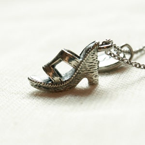 May include: A silver charm necklace featuring a detailed, three-dimensional charm of a high-heeled sandal.