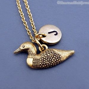 May include: Gold necklace featuring a loon charm and a gold initial charm. The initial charm has the letter "J" on it.