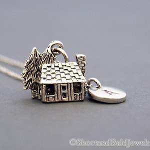 May include: Silver charm necklace featuring a small cabin with a tree and a round charm with the letter A.