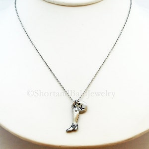 May include: A silver chain necklace with a charm of a silver boot and a silver charm with the letter K.
