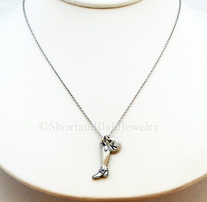 May include: A silver chain necklace with a charm of a silver boot and a silver charm with the letter K.