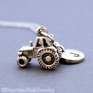 May include: Silver charm of a detailed tractor with a silver initial charm attached. The initial charm is the letter J.
