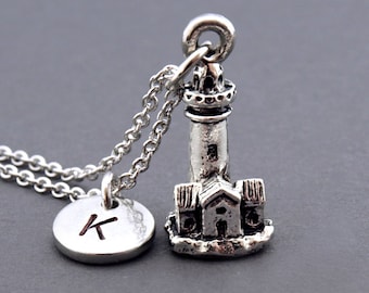 May include: Silver necklace featuring a lighthouse charm and a round charm with the letter K.