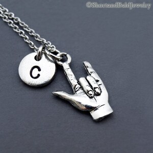 May include: Silver necklace with a charm that says "I love you" in American Sign Language and a silver disc charm with the letter "C" on it.