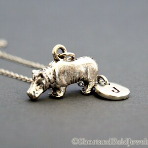 May include: Silver hippopotamus charm necklace with a silver initial charm. The initial charm has the letter "J" on it.