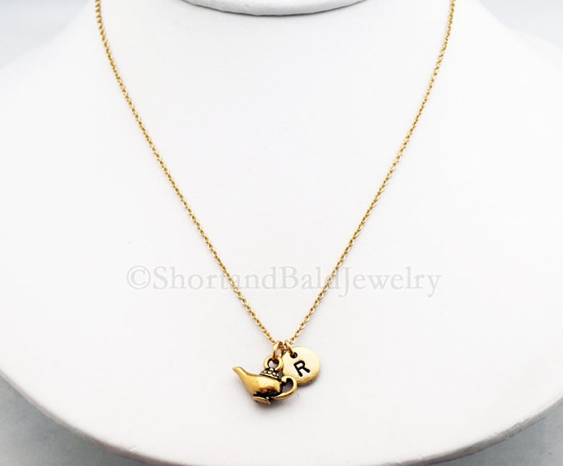 Puede incluir: Collar de cadena dorada con un dije de l&aacute;mpara de genio dorada y un dije inicial dorado con la letra "R".