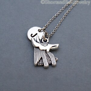May include: Silver necklace with a charm of an Anubis head and a round charm with the letter J.