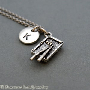 May include: Silver necklace with a pool table charm and a letter K charm. The necklace is on a gray background.