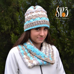 May include: A crocheted hat and scarf set in shades of beige, white, and light blue. The hat has a textured stitch pattern and the scarf is a cowl style.