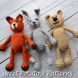 May include: Three crocheted stuffed animals: a fox, a rabbit, and a bear. The fox is orange with a white tail tip, the rabbit is gray, and the bear is beige.  The animals are sitting on a white wooden surface.  Sweet Potato 3 Patterns.