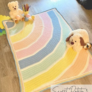 May include: A rainbow crochet baby blanket with a white border. The blanket is made with a variety of pastel colors, including pink, blue, yellow, and green. The blanket is laid out on a wooden floor with two stuffed animals, a bear and a dog, sitting on it. The text "Sweet Potato 3" is written in cursive on the floor below the blanket.