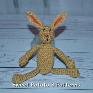 May include: A crocheted brown bunny rabbit with orange ears. The bunny is sitting on a wooden surface. The text "Sweet Potato 3 Patterns" is visible at the bottom of the image.