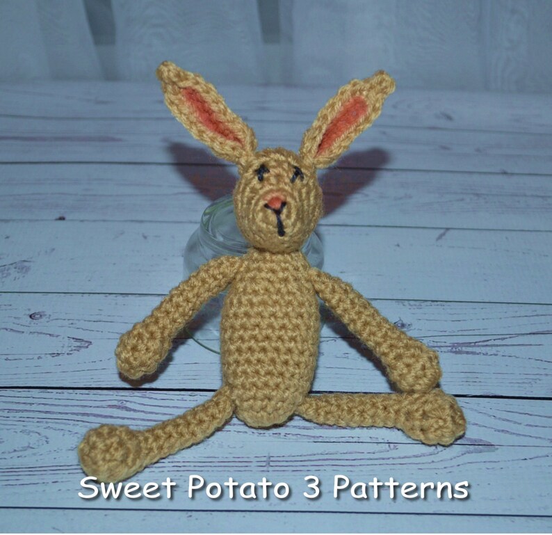 May include: A crocheted brown bunny rabbit with orange ears. The bunny is sitting on a wooden surface. The text "Sweet Potato 3 Patterns" is visible at the bottom of the image.