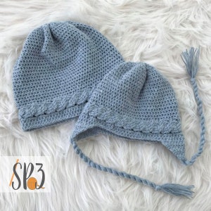 May include: Two crocheted hats in a light blue color. One hat has a long tassel and the other hat has a shorter tassel. Both hats have a braided trim around the brim.