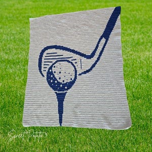 Könnte beinhalten: Eine gehäkelte Decke mit einem marineblauen Golfschläger- und Golfball-Design auf hellgrauem Hintergrund. Die rechteckige Decke scheint handgefertigt zu sein. Der Text "Sweet Potato 3" befindet sich in der unteren linken Ecke.