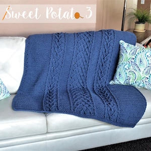 Peut inclure: Une couverture en crochet bleu avec un motif en tricot torsadé, drapé sur un canapé blanc. Le texte "Sweet Potato 3" est visible en arrière-plan.