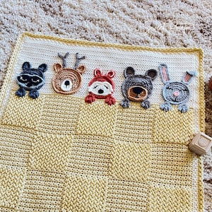 May include: A crocheted baby blanket with a yellow and white checkered pattern. The blanket features five appliqued animal faces: a raccoon, a deer, a fox, a bear, and a rabbit.