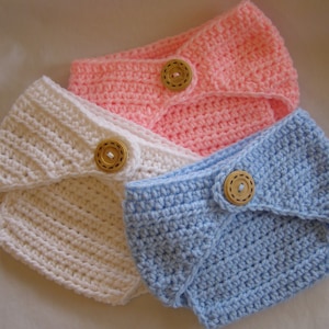May include: Three crocheted baby diaper covers, one white, one pink, and one light blue, each with a wooden button.