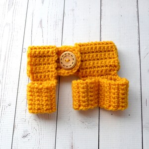 May include: A yellow crocheted baby romper with a wooden button. The romper has a wide waistband and leg openings.