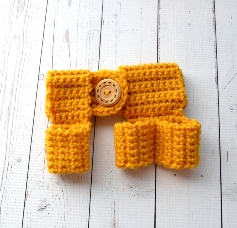 May include: A yellow crocheted baby romper with a wooden button. The romper has a wide waistband and leg openings.