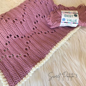 May include: A crocheted baby blanket in a dusty rose color with a white crocheted border. The yarn is labeled "Mary Maxim Best Value" and is 6 oz / 170 g, 342 yds / 313 m. The blanket is labeled "Sweet Potato 3".