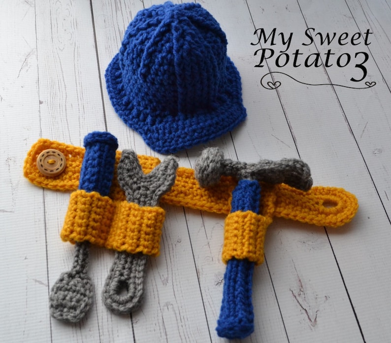 May include: A blue crocheted construction worker hat with a yellow crocheted tool belt with a screwdriver, wrench, and hammer.