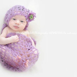 May include: A newborn baby wrapped in a purple crocheted blanket and wearing a matching crocheted hat with a purple flower.
