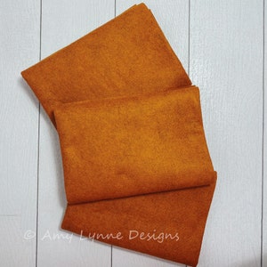 May include: Three pieces of orange felt fabric folded on top of each other. The felt is a deep orange color.
