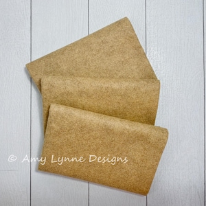 May include: Three pieces of brown felt fabric folded on top of each other. The fabric is a light brown color and has a slightly textured surface.
