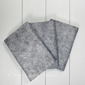 May include: Three pieces of gray felt fabric folded together on a white wooden surface.