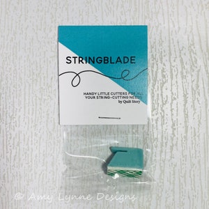 May include: A turquoise blue string cutter with the text "STRINGBLADE" and "HANDY LITTLE CUTTERS FOR ALL YOUR STRING-CUTTING NEEDS by Quilt Story" on the packaging.