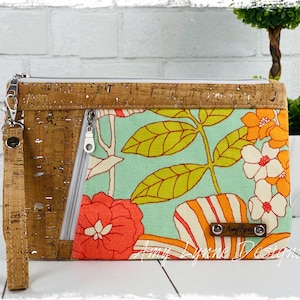 May include: A rectangular wristlet clutch featuring a natural cork exterior with silver flecks and a light blue fabric panel with a vibrant floral print in orange, yellow, and white. It includes a silver zipper, a wrist strap, and a brown label.