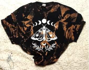 May include: Black bleached t-shirt with a white moth and moon phases graphic. The graphic features a moth with spread wings and a crescent moon with five phases.
