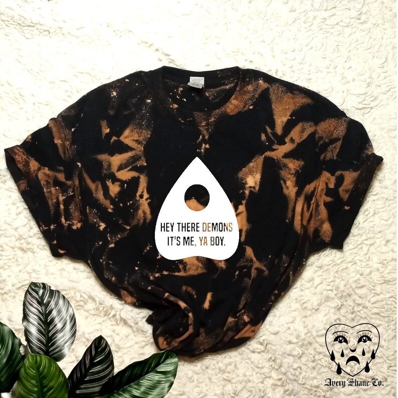 May include: Black t-shirt with a brown bleach tie-dye pattern. The shirt features a white graphic of a ghost with the text "Hey there demons it's me, ya boy."