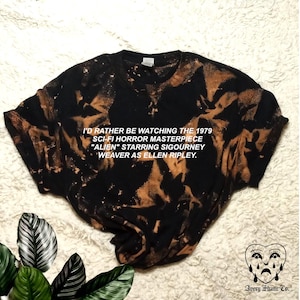 May include: Black t-shirt with a bleach-splattered design. The text "I'd rather be watching the 1979 sci-fi horror masterpiece "Alien" starring Sigourney Weaver as Ellen Ripley." is printed in white on the shirt.