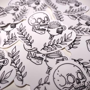 May include: A set of black and white stickers featuring a skull holding a cup of coffee. The stickers have a simple line art style and include the text "Avery Stone Co.".