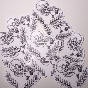 May include: A set of black and white stickers featuring a skull holding a cup of coffee. The stickers are on a white background and have a simple, minimalist design.