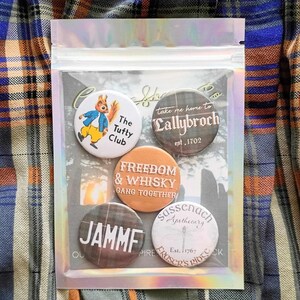 May include: Set of six round button pins with various designs. The pins feature a cartoon squirrel, a plaid pattern with the text "Take me home to Lallybroch est. 1702", a plaid pattern with the text "Freedom & Whisky Gang Together", a plaid pattern with the text "Jammf", a white background with the text "Sassenach Apothecary Est. 1767", and a plaid pattern with the text "Fraser's Ridge".