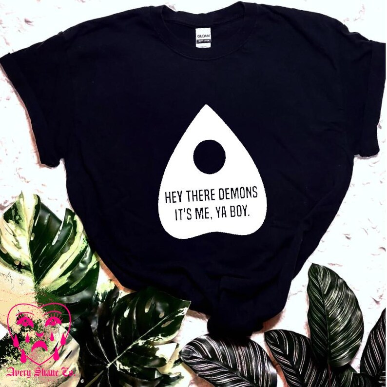 May include: Black t-shirt with a white graphic of a Ouija board planchette with the text "Hey there demons it's me, ya boy."