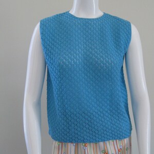 May include: A sleeveless, blue, knitted top with a round neckline. The top is made of a textured, open-weave fabric.