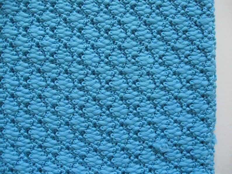 May include: A close-up of a blue textured fabric with a diamond pattern. The fabric is woven with a raised texture.