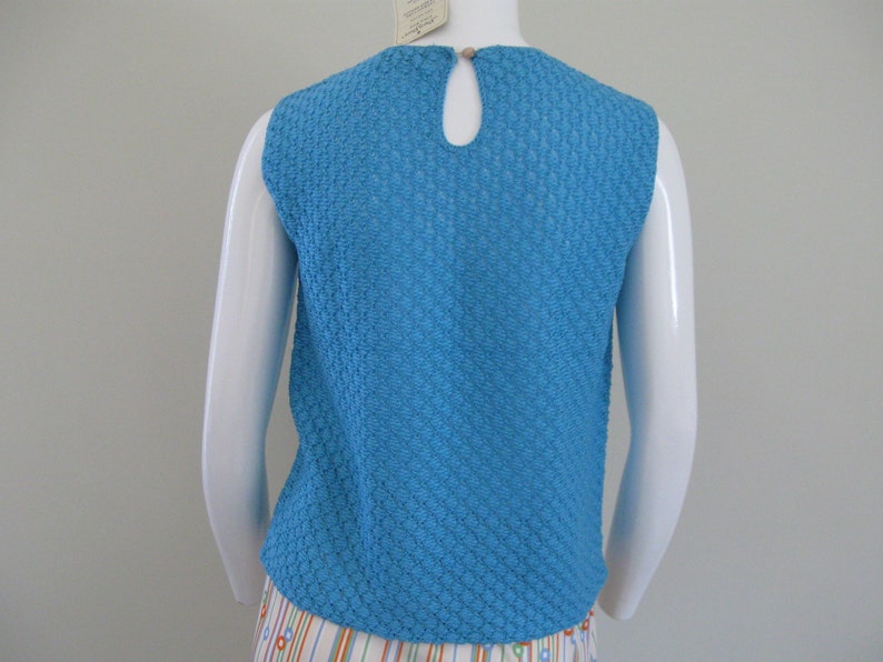 May include: A sleeveless, blue, textured knit top with a round neckline. The top has a keyhole opening in the back.
