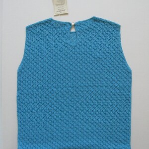 May include: A sleeveless, light blue knitted top with a diamond pattern. The top has a small, round button at the back of the neck.