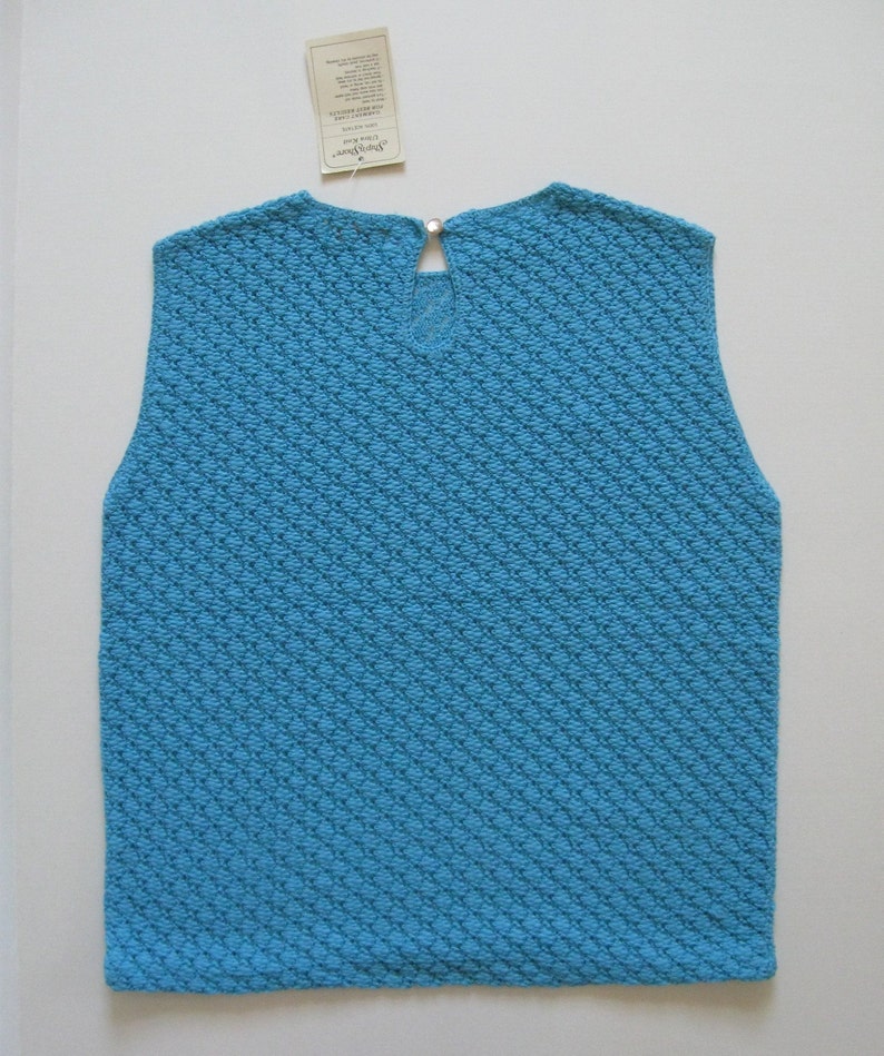 May include: A sleeveless, light blue knitted top with a diamond pattern. The top has a small, round button at the back of the neck.