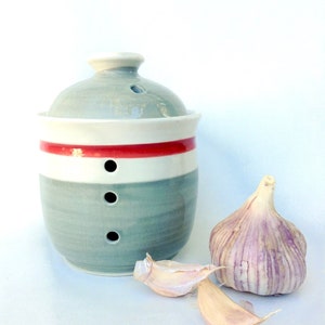 May include: A ceramic garlic keeper with a lid, painted in shades of blue, white, and red. The keeper has three ventilation holes and is next to a bulb of garlic and two cloves.