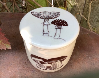May include: White ceramic butter dish with a brown mushroom design. The lid has two mushrooms with brown stems and white caps with brown spots. The bottom of the dish has three mushrooms with brown stems and white caps.