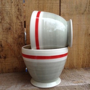 Könnte beinhalten: Zwei graue Keramikschalen mit roten und weißen Streifen. Die Schalen sind übereinander gestapelt.